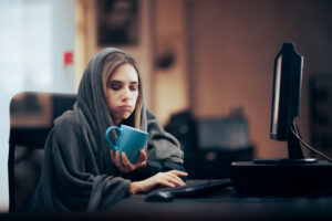 Sick worker with blanket and a cup of tea while working at her office